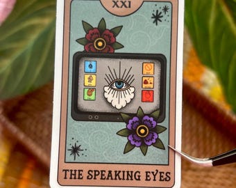 May include: A tarot card sticker featuring a stylized eye on a tablet screen, surrounded by floral accents. The card is labeled "XXI" at the top and "THE SPEAKING EYES" at the bottom. The sticker has a light blue background with a beige border.