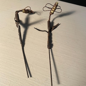 May include: Two handmade, rustic hair sticks. One features a coiled, dark brown stem with a decorative top. The other has a similar stem with a spiral design and a small, decorative top. Both are on a white surface.
