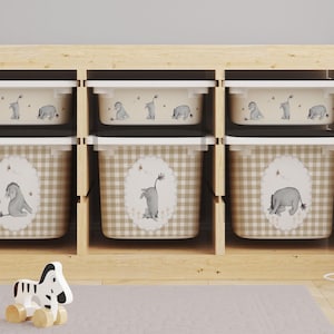 Puede incluir: Un mueble de almacenamiento de madera con seis cubículos, cada uno con un contenedor de almacenamiento blanco y beige. Los contenedores presentan un patrón de cuadros y etiquetas ovaladas con ilustraciones de burros grises. Los contenedores superiores tienen tapas.