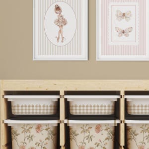 Peut inclure: Deux cadres avec une ballerine et des papillons au-dessus de bacs de rangement. L'impression de la ballerine est ovale avec un fond rayé beige et blanc. L'impression de papillon a un fond rayé rose et blanc. Les bacs de rangement ont des motifs floraux et vichy.