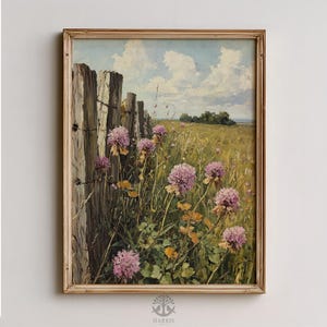 May include: A framed landscape painting shows a field of wildflowers and a weathered wooden fence under a blue sky with clouds. The artwork features pink flowers and a golden frame.
