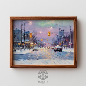 May include: A framed art print of a winter cityscape. The painting shows a snow-covered street with cars, traffic lights, and buildings under a colorful sky. The artwork is in a wooden frame. The print is from Harris Prints.