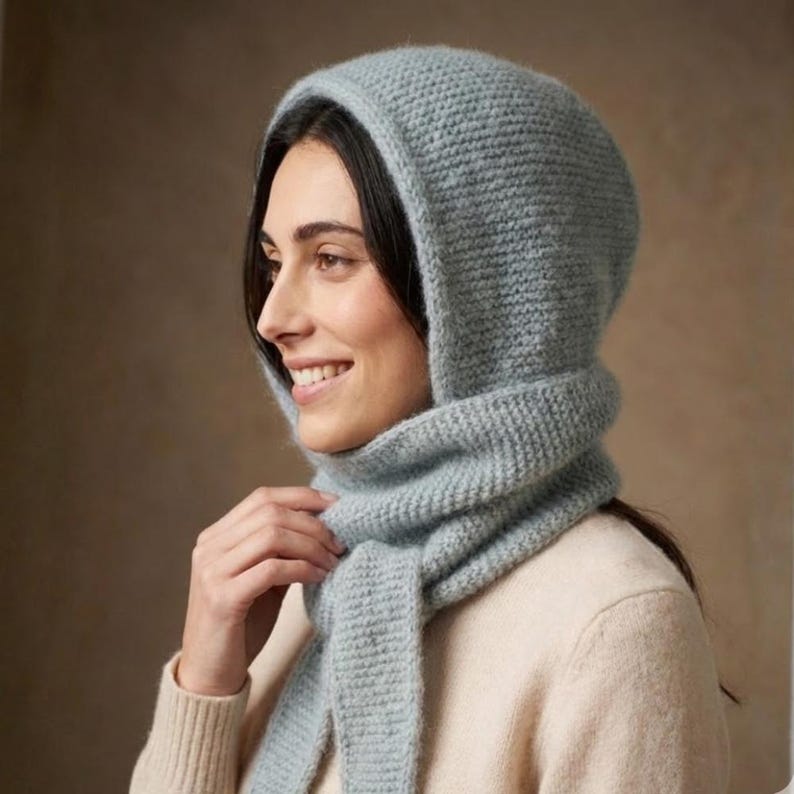 May include: A light blue knitted hood and scarf set. The hood covers the head and neck, with a scarf that can be wrapped around the neck. The set is made of a soft, textured yarn, ideal for cold weather.