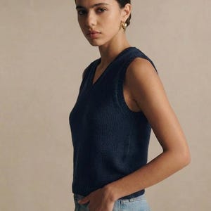 Puede incluir: Un chaleco sin mangas de punto azul marino con cuello en V. El chaleco est&aacute; hecho de un material de punto y se combina con vaqueros azul claro. La modelo lleva pendientes dorados.