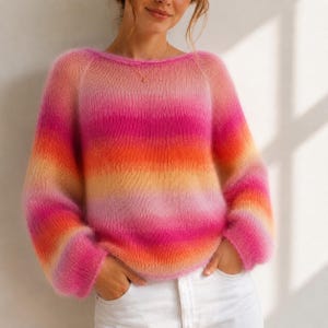 Könnte beinhalten: Ein langärmeliger, flauschiger Strickpullover mit einem horizontalen Farbverlauf in leuchtendem Pink, hellem Orange und sanftem Gelb. Das Kleidungsstück hat einen weiten, abgerundeten Ausschnitt und eine lockere, bequeme Passform.