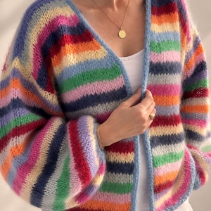May include: A chunky knit cardigan featuring horizontal stripes in vibrant shades of pink, orange, yellow, green, light blue, and dark blue. The garment has a V-neckline, long sleeves with dropped shoulders, and a light blue trim along the front opening.