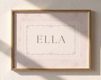 May include: A rectangular wall art print in a gold frame featuring the name ELLA in dark brown capital letters centered within a decorative border on a pale pink background with a subtle floral pattern.