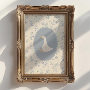 Może przedstawiać: Oprawiony wydruk z ilustracją białej gęsi w niebieskim owalu, na tle kwiatowym. Ozdobna złota rama dodaje stylu vintage. Grafika jest zamontowana na białej ścianie, z cieniami.