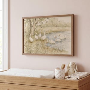 May include: A rectangular framed wall art print featuring a watercolor illustration of six white geese near a pond. The scene includes a large tree on the left bank, grassy vegetation, and soft muted earth tones throughout the landscape composition.