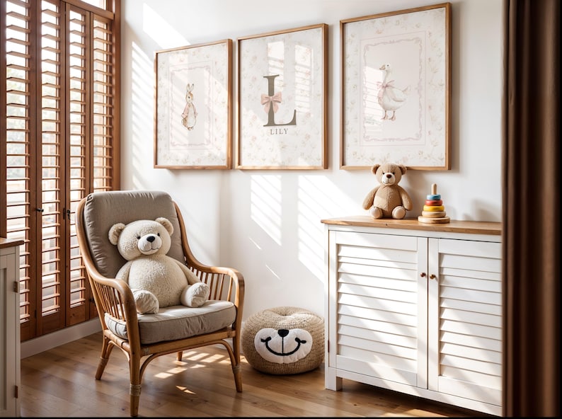 May include: A nursery room featuring a rattan armchair with a beige cushion and a teddy bear, a white louvered cabinet with a wooden top, a round bear-faced floor cushion, and three framed wall prints depicting a rabbit, the letter L, and a goose.