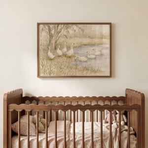 May include: A framed watercolor print featuring a group of white geese near a pond and a tree, displayed above a wooden crib with a scalloped top rail. The artwork uses soft, muted tones of green, brown, and blue to depict a natural landscape.