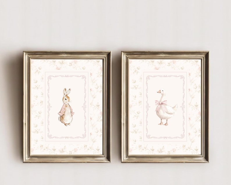 May include: Two framed wall art prints featuring watercolor illustrations. The left print shows a brown rabbit wearing a pink jacket. The right print shows a white goose with a pink bow. Both prints have a light pink floral border and ornate frames.