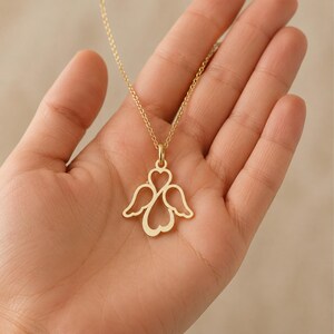 May include: A gold-toned necklace featuring a pendant shaped like a stylised angel with wings and a heart-shaped body. The pendant is suspended from a delicate gold-toned chain, showcasing a cut-out design that forms the silhouette of an angel.