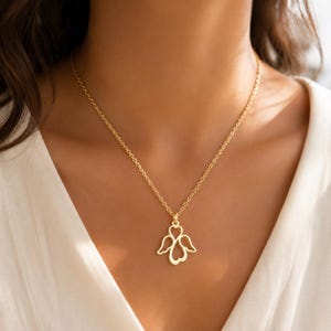 May include: A gold-toned necklace featuring a delicate chain and a pendant shaped like an angel with heart-shaped wings. The pendant is constructed from thin, polished metal wire, creating an openwork design that hangs centrally from the chain.