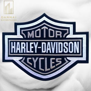 May include: A black and silver Harley-Davidson Cycles patch. The patch features the Harley-Davidson logo with the words "MOTOR HARLEY-DAVIDSON CYCLES" in white and silver stitching. The patch has a black border and is on a white background.