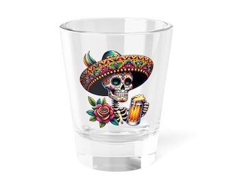 May include: A clear shot glass featuring a colorful Day of the Dead design. The image depicts a skeleton wearing a sombrero and holding a mug of beer, with a rose and leaves. The design is vibrant with multiple colors.
