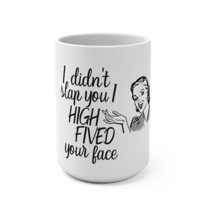 May include: White ceramic mug with the text "I didn't slap you I HIGH FIVED your face" in black. A retro illustration of a woman is on the right side of the mug. The mug is a novelty item.