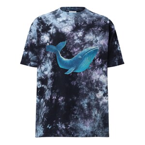 May include: A short-sleeved t-shirt with a tie-dye pattern in shades of black, blue, and purple. A blue whale graphic is centered on the front. The shirt has a crew neck and a relaxed fit.
