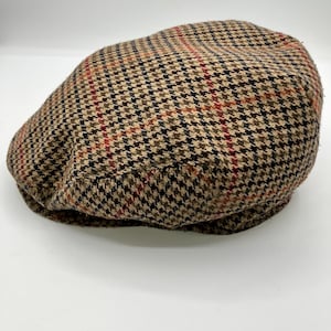 May include: A brown and black houndstooth pattern newsboy cap. The cap features a classic design with a rounded crown and a small, stiff brim. The fabric has accents of red and tan.