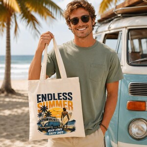 May include: A cream-colored canvas tote bag featuring a graphic print with the text ENDLESS SUMMER and GOOD VIBES SALTY DAYS. The illustration depicts a blue van, palm trees, a sunset, and a person holding a surfboard on a sandy beach.