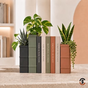 May include: A collection of rectangular planters and book-shaped containers in shades of charcoal, olive, cream, and terracotta. The containers feature text including Form & Function, The Quiet Home, Material Studies, Objects in Place, and Simple Rituals.