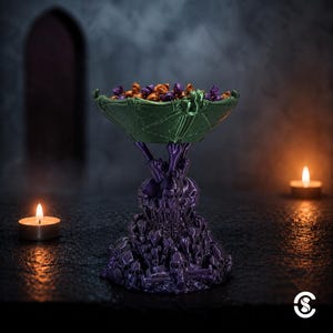 May include: A decorative bowl featuring a green, textured basin supported by a base composed of stacked purple skulls and bones. The bowl is filled with small, shiny orange and purple candies, creating a distinct contrast between the dark base and top.