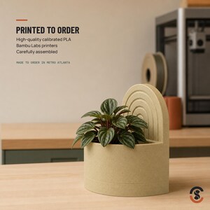 A light beige bookend planter with a small green plant, with text overlay "PRINTED TO ORDER High-quality calibrated PLA Bambu Labs printers Carefully assembled MADE TO ORDER IN METRO ATLANTA."