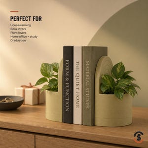 Two light green, curved bookends with planters holding green leafy plants, flanking three books on a wooden surface, with a gift box in the background.