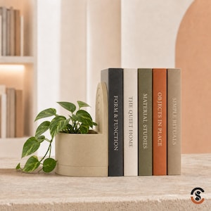 May include: A beige arched planter with a green pothos plant positioned next to five books titled Form & Function, The Quiet Home, Material Studies, Objects in Place, and Simple Rituals, featuring spines in black, white, olive, terracotta, and tan.