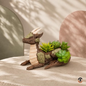 May include: A brown dragon-shaped planter with a cream-colored underbelly, two horns, and textured scales. The back of the dragon features multiple openings containing various green artificial succulent plants with different leaf shapes and sizes.
