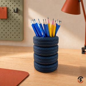 May include: A dark blue pencil holder shaped like a stack of four tires. The cylindrical container is filled with several sharpened pencils featuring blue, yellow, and white casings. The tire-themed organizer has a textured tread pattern.