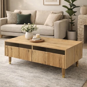 Peut inclure: Une table basse en bois clair avec un panneau avant texturé et des accents sombres. La table a quatre pieds avec des embouts dorés. Un vase de fleurs blanches et une bougie sont posés dessus.