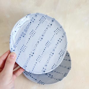 Puede incluir: Dos platos de cer&aacute;mica azul claro con un patr&oacute;n de puntos en azul m&aacute;s oscuro. Los platos son redondos y tienen una textura moteada. Un plato se sostiene ligeramente por encima del otro, mostrando el dise&ntilde;o.