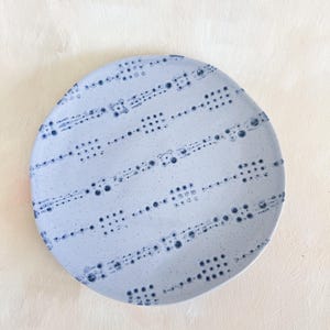 Puede incluir: Un plato redondo de cer&aacute;mica azul claro con un patr&oacute;n de puntos azul oscuro. El dise&ntilde;o presenta filas de peque&ntilde;os puntos y puntos m&aacute;s grandes agrupados, creando una apariencia texturizada. El plato tiene un borde ligeramente irregular.