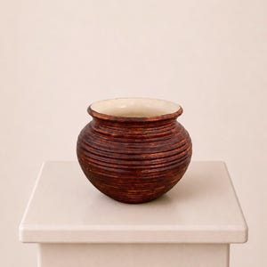 Peut inclure: Un petit pot en céramique rond avec un extérieur brun foncé à nervures horizontales et un intérieur lisse de couleur crème. Le récipient présente un bord large et légèrement évasé ainsi qu'un corps bombé, avec une texture uniforme.