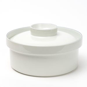 May include: A white ceramic lidded container with a cylindrical base and a matching circular lid featuring a small, raised central knob. The vessel has a smooth, glossy finish and a simple, uniform design, presenting a clean and functional appearance.