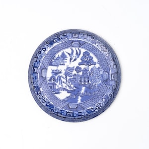 Puede incluir: Una taza de cerámica blanca con asa negra y el texto "But First, Coffee" en negrita negra. La taza se encuentra sobre un fondo borroso, sugiriendo un ambiente acogedor.