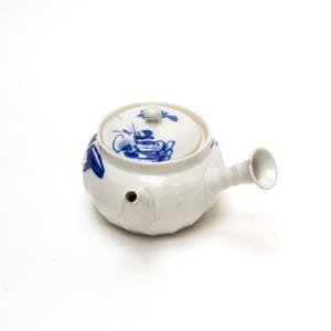 May include: A white ceramic teapot with a lid, spout, and handle. The teapot is decorated with blue floral designs. The spout is a small, round shape. The handle is a small, round shape. The lid has a small knob.