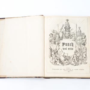 May include: Open antique book with the title "Punch vol xxiv" on the right page. The illustration features numerous figures in a detailed, black and white drawing. The book's cover is dark with visible wear.