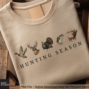Puede incluir: Una sudadera beige de cuello redondo con un estampado gráfico de un ánade real, un ciervo, un pavo, un pez y un uapití. El texto "HUNTING SEASON" está impreso en letras mayúsculas negras debajo de las ilustraciones de los animales.