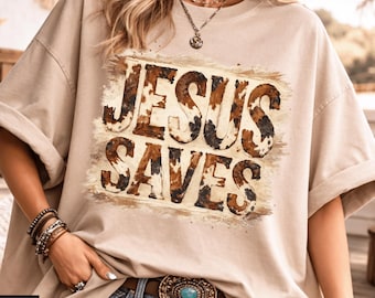May include: A beige t-shirt featuring the text "JESUS SAVES" in a brown and white cowhide pattern. The shirt has rolled-up sleeves and is paired with blue jeans and a decorative belt. The image includes the "SJOY STUDIO" logo.