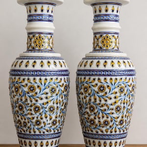 K&ouml;nnte beinhalten: Ein Paar passende wei&szlig;e Keramikvasen mit aufwendigen, handbemalten Blumenmustern in Blau- und Goldt&ouml;nen. Das Design umfasst sich wiederholende Bl&uuml;tenblattmotive, geschwungene Ranken und kleine kreisf&ouml;rmige Akzente am Hals und Fu&szlig;.
