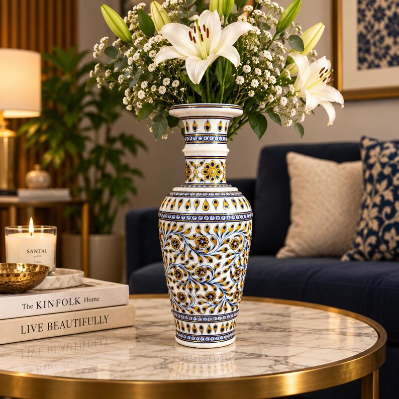 K&ouml;nnte beinhalten: Eine hohe, wei&szlig;e Keramikvase mit einem komplexen, handbemalten Muster aus blauen und gelben Blumenmotiven und tropfenf&ouml;rmigen Elementen. Die Vase hat einen ausgestellten Rand, einen schlanken Hals und einen bauchigen K&ouml;rper, gef&uuml;llt mit wei&szlig;en Lilien.