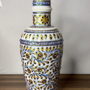 K&ouml;nnte beinhalten: Eine Vase aus wei&szlig;em Marmor mit handgemalten floralen Mustern in Gold und Blau. Die Oberfl&auml;che ist mit kleinen, eingelassenen klaren Kristallen verziert, die in B&auml;ndern und in den Mitten der gemalten Blumen angeordnet sind und ein Dekor bilden.