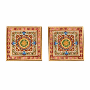 May include: Two square coasters featuring a central floral mandala design in yellow, green, and blue, surrounded by a red border with white and gold geometric patterns and small blue bird motifs, finished with a gold-toned outer edge.