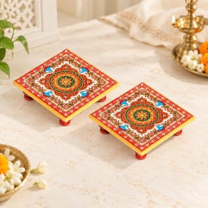 May include: Two square wooden platforms with four small red feet each. The tops feature a vibrant, symmetrical floral pattern in shades of red, orange, green, and blue, accented with white dots and intricate gold-toned decorative borders.