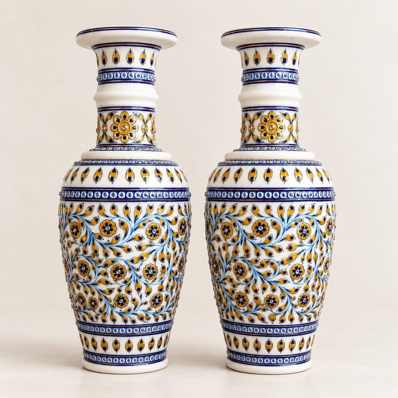 K&ouml;nnte beinhalten: Ein Paar hohe, wei&szlig;e Keramikvasen mit aufwendigen, handbemalten Blumenmustern in Gelb-, Blau- und Goldt&ouml;nen. Das Design umfasst sich wiederholende Blattmotive, kleine Bl&uuml;ten sowie geometrische Bord&uuml;ren am Hals und am Fu&szlig; der Vasen.