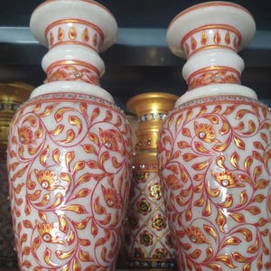 K&ouml;nnte beinhalten: Zwei Vasen aus wei&szlig;em Marmor mit handgemalten, gold-roten floralen Rankenmustern. Jede Vase hat einen ausgestellten Rand, einen bauchigen K&ouml;rper und ist mit kleinen, klaren eingelegten Steinen am Hals und am Fu&szlig; verziert.