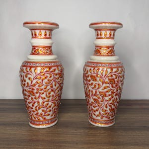 K&ouml;nnte beinhalten: Ein Paar Vasen aus wei&szlig;em Marmor mit handgemalten roten und goldenen Blumenrankenmustern. Die Vasen sind mit kleinen eingelegten Kristallen am Hals und K&ouml;rper verziert und weisen einen ausgestellten Rand sowie eine konische Form auf.