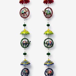 May include: Two decorative hanging ornaments featuring colorful elephant designs. Each ornament has a series of elements: a red umbrella, an elephant in a ring, a yellow umbrella, another elephant in a ring, a blue umbrella, and a gold bell.